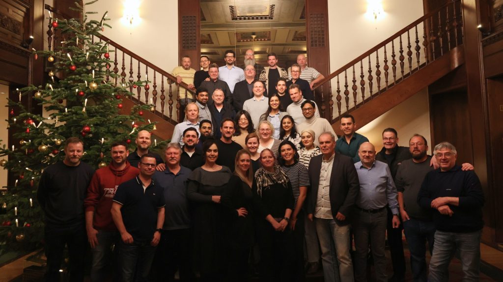 Mitarbeitende der redi-Group stehen gemeinsam vor einem geschmückten Weihnachtsbaum in einem historischen Treppenhaus.